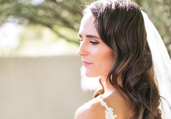 Brunette girl in a wedding dress and veil looking away from the camera while standing outside.